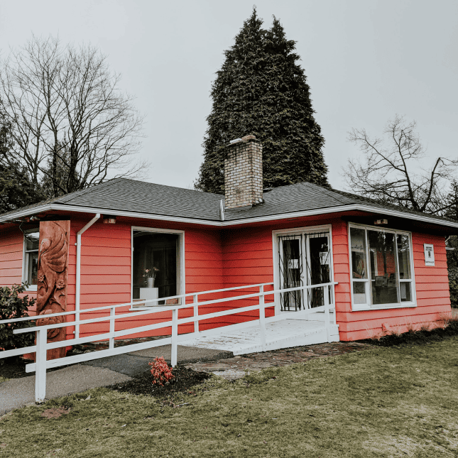 Small red heritage-style building surrounded by grass and trees.