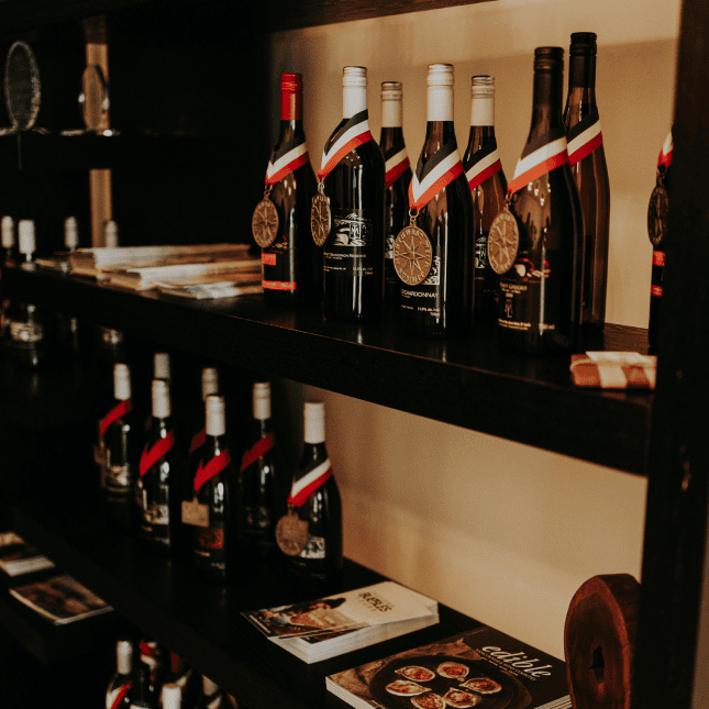 Wine bottles are displayed on shelves inside a warmly lit tasting room.