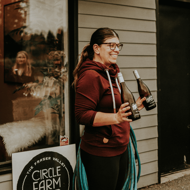 Person holding a glass of wine while standing outside a winery building.