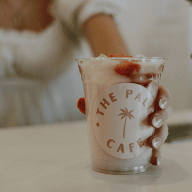 Hand holding a branded café cup filled with a beverage.