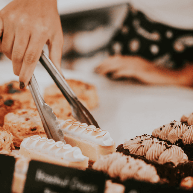 Hand using tongs to select pastries from a bakery display.