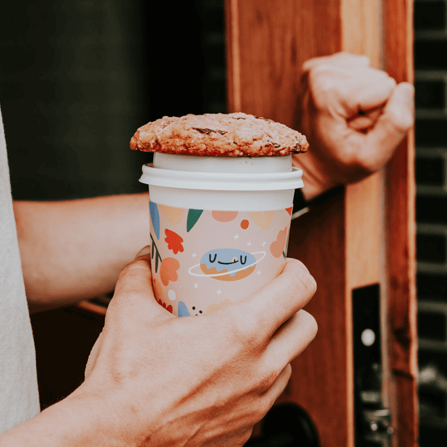 Person holding a colorful cup topped with a cookie.
