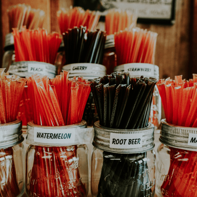 Close-up of assorted red and black honey sticks in labeled glass jars.