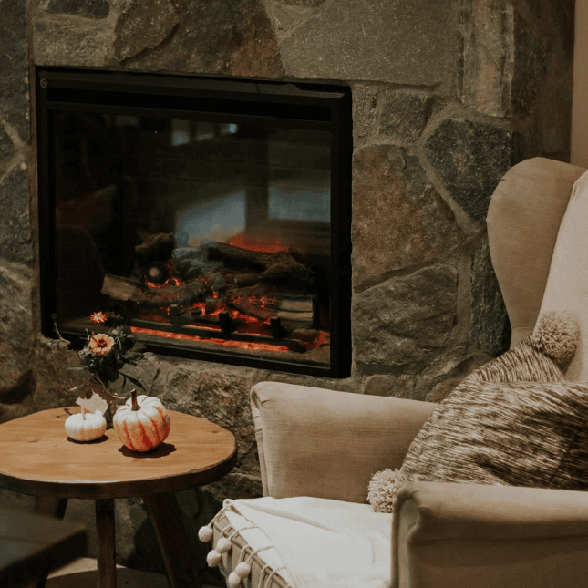 Cozy seating area beside a lit fireplace with a coffee and dessert on a small table.
