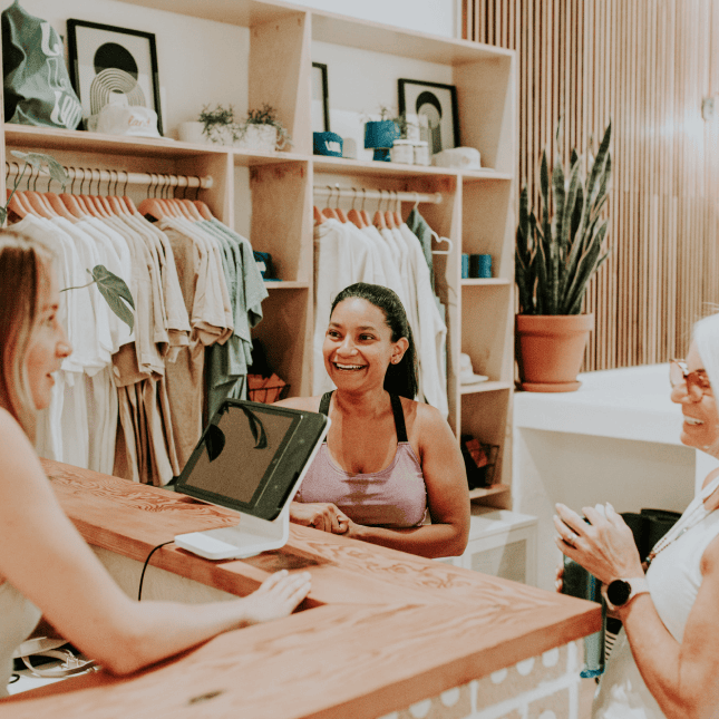 A shop owner smiles behind a counter while assisting a customer