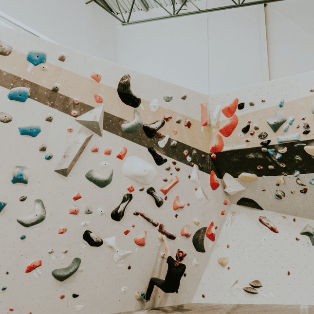 A climber scaling an indoor wall with multicolored holds.