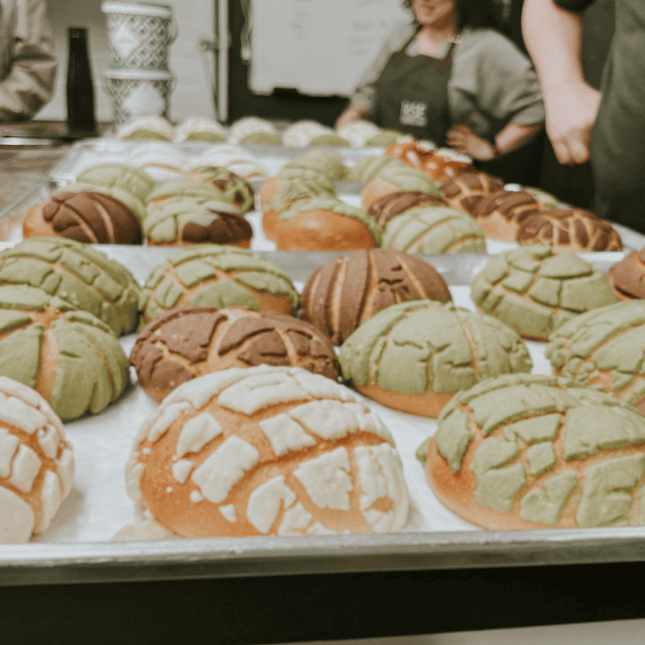Tray of round loaves topped with decorative icing patterns in a bakery kitchen.