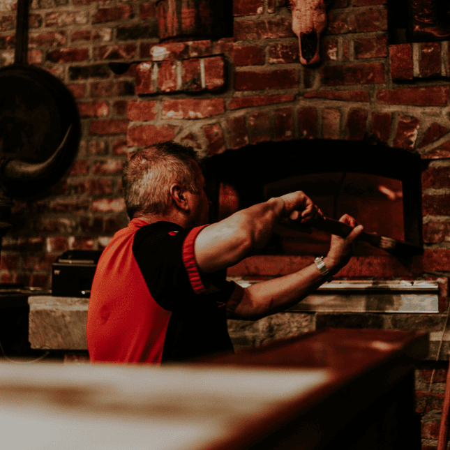 A chef placing or removing food from a wood-fired oven in a brick kitchen.