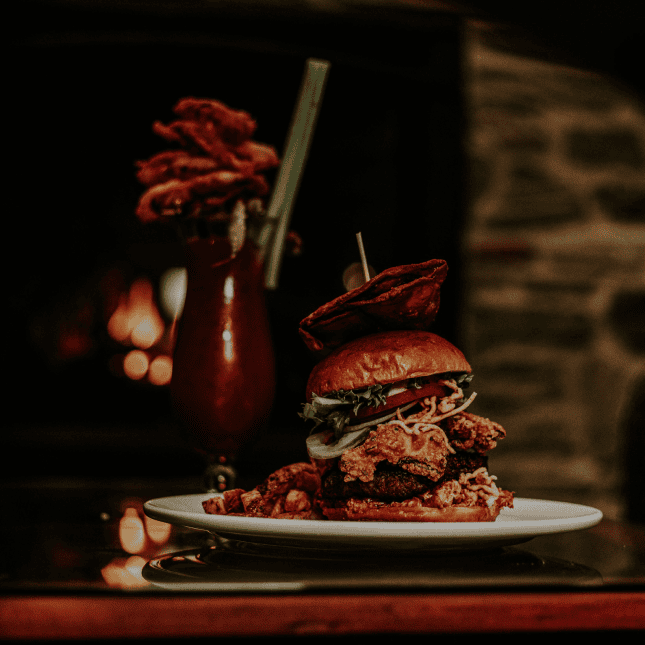 A plated gourmet dish with stacked ingredients and garnish, dramatically lit against a dark background.