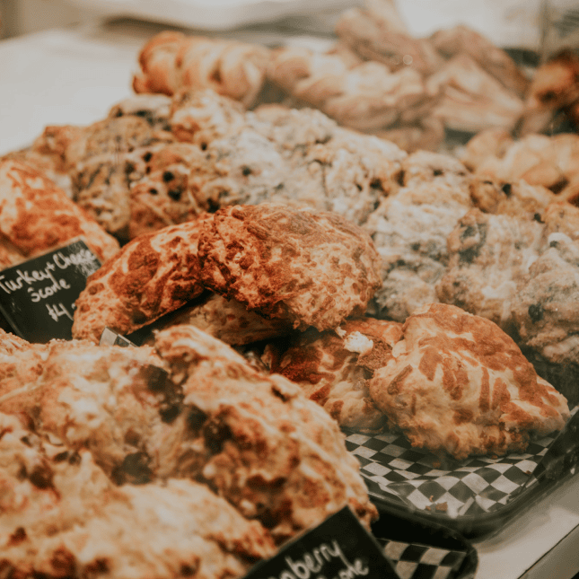 Close-up of golden-brown crumb-topped scones arranged in a bakery display.
