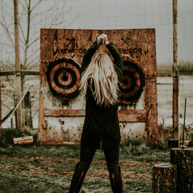 A person standing outdoors throwing an axe at a wooden target mounted on a wall.