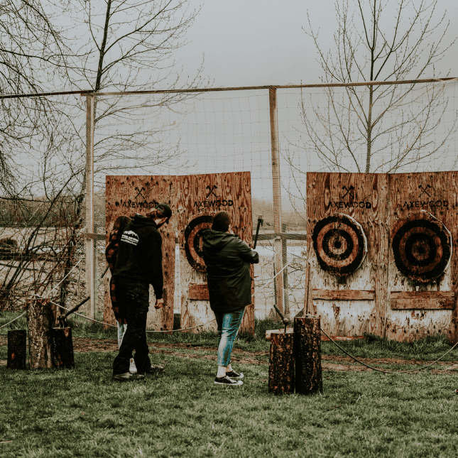 Two people participating in axe throwing, facing multiple wooden targets in an outdoor range.