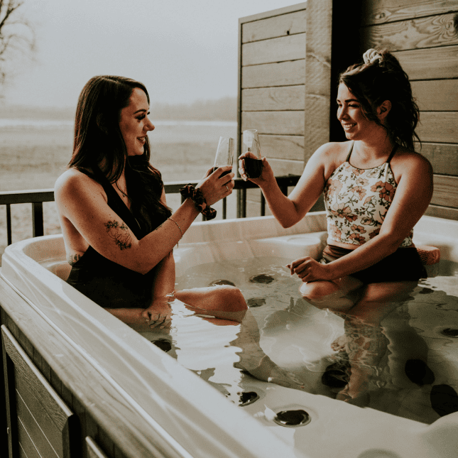 wo people relaxing in an outdoor hot tub, holding drinks and talking.