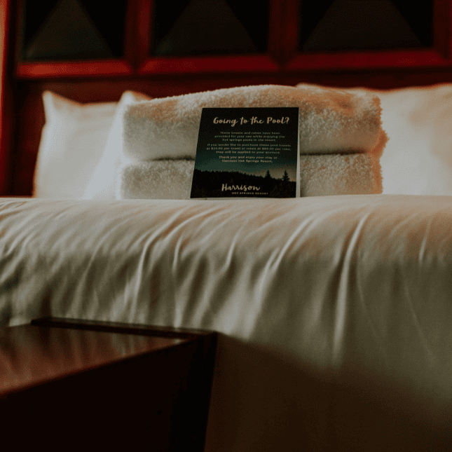 Close-up of a hotel bed with crisp white linens and a folded card placed on top.