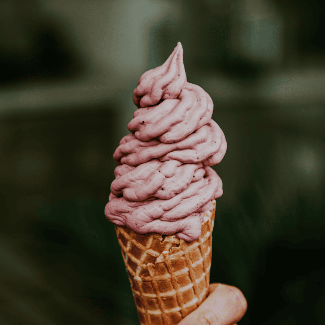 Pink soft-serve ice cream swirled into a waffle cone held outdoors.