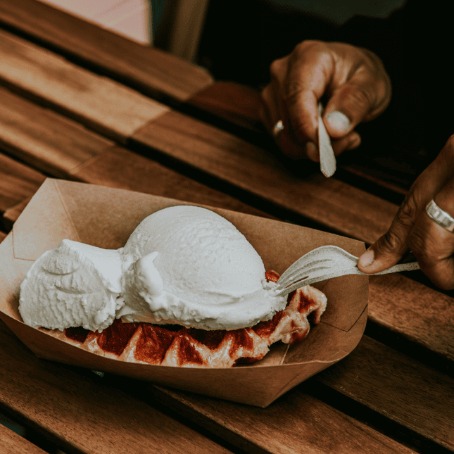 Scoops of vanilla ice cream served on a dessert, with a spoon resting on a wooden table.