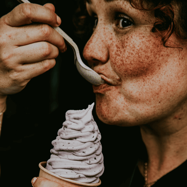 Person tasting a dessert with a spoon at an outdoor café.