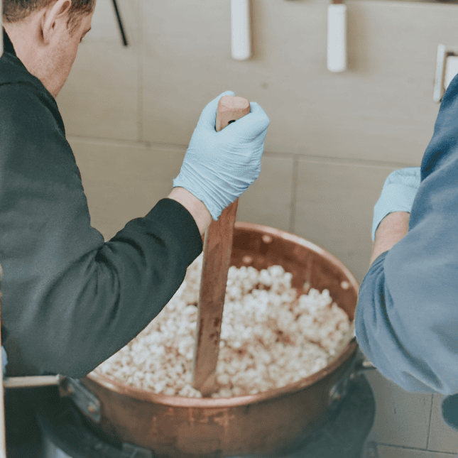 Hands mixing popcorn in a large bowl inside a bakery kitchen.