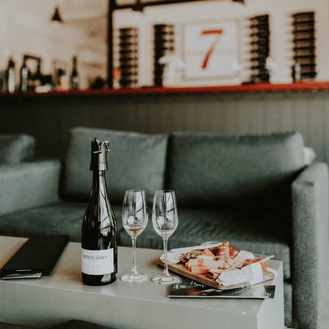 A bottle of wine and two wine glasses on a coffee table beside a charcuterie board, with a couch in the background.