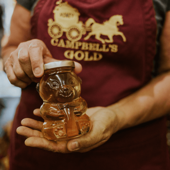 Person holding a small jar of honey inside a farm shop.
