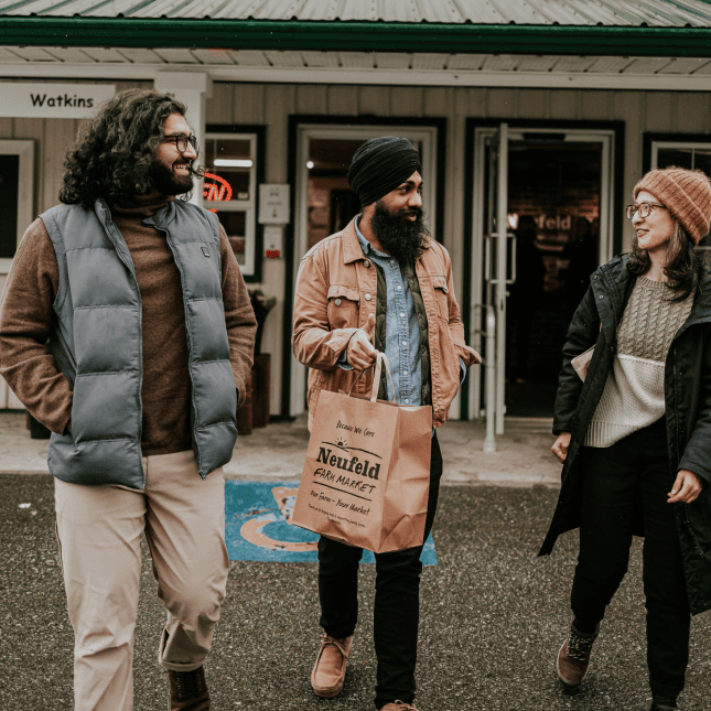 Three people walking outside a market carrying shopping bags.