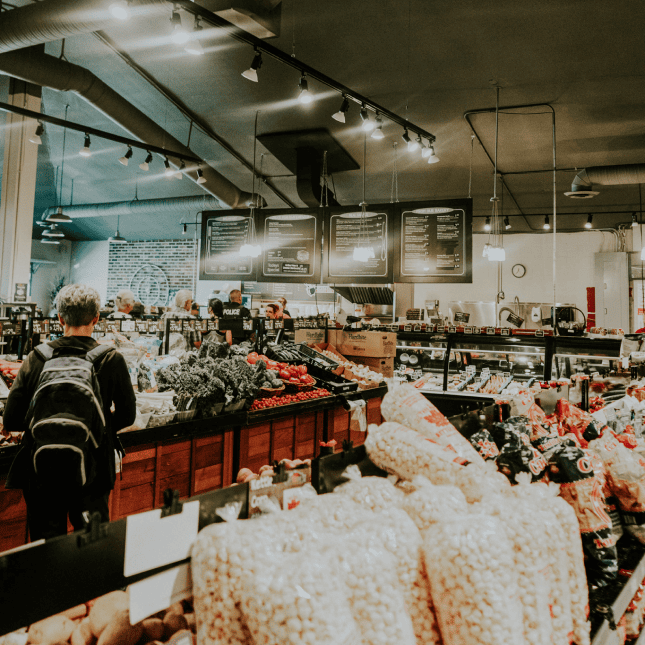 Busy indoor farm market with shoppers and produce displays.