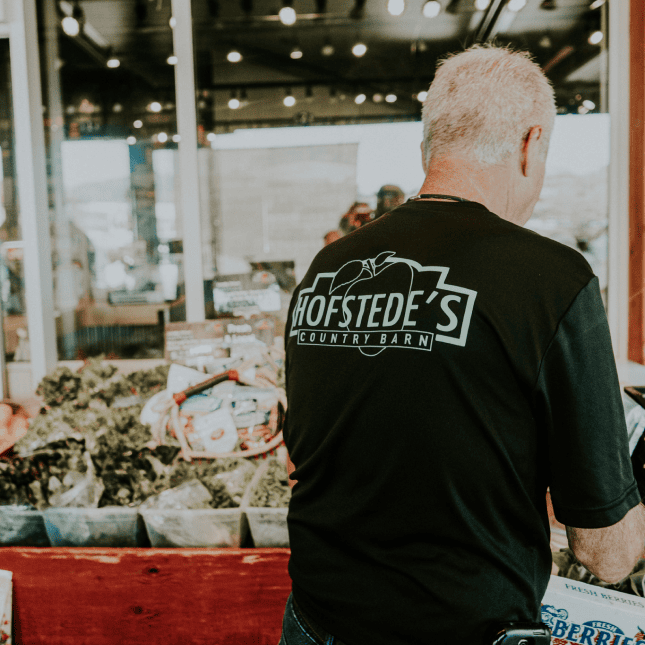 Person walking through a market wearing a branded shirt.