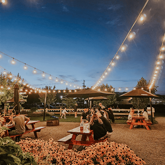Outdoor brewery patio at night with string lights and seating.