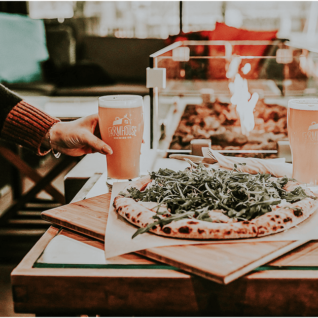 Pizza and drinks served on a wooden table at a brewery.