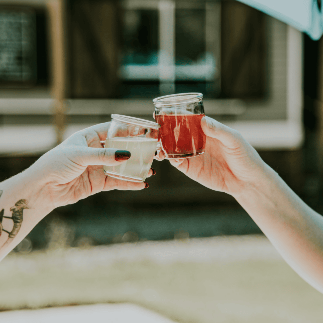 Two people clinking glasses of cider outdoors.