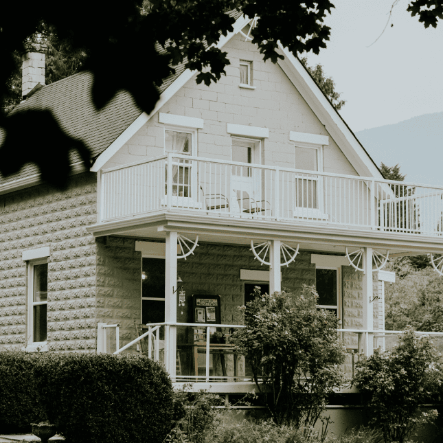 Exterior of a white farmhouse surrounded by greenery.