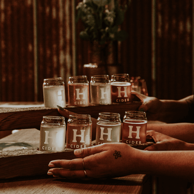Hands holding small bottles of handcrafted cider.