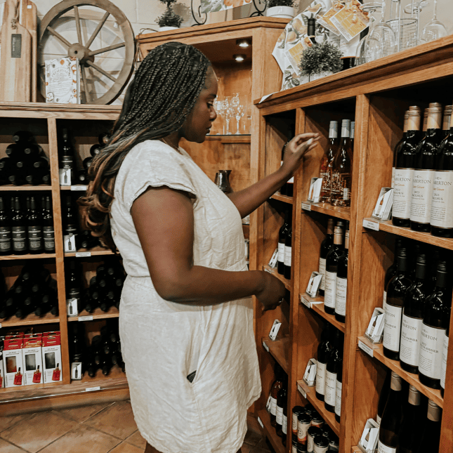 Person browsing wine bottles on wooden retail shelves.