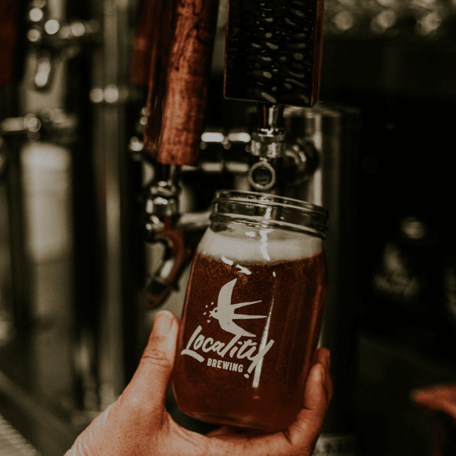Glass of amber craft beer with brewing equipment in background.