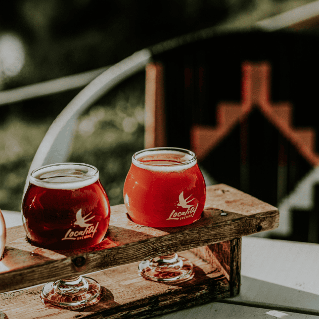 Two glasses of red craft beer on a wooden table outdoors.