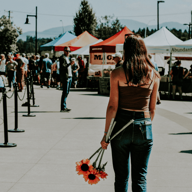 a girl holding flowers walking into an outdoor market